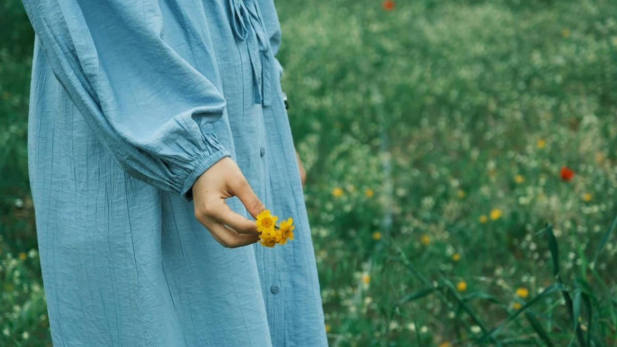 A serene image of a person in a blue dress holding bright yellow flowers in a lush green field.