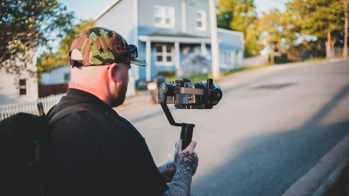 Tattooed photographer filming a suburban street with a camera stabilizer.