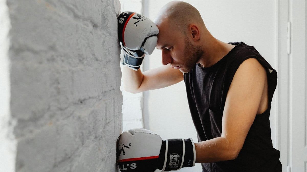 A man in boxing gloves resting against a wall, representing fatigue and determination.