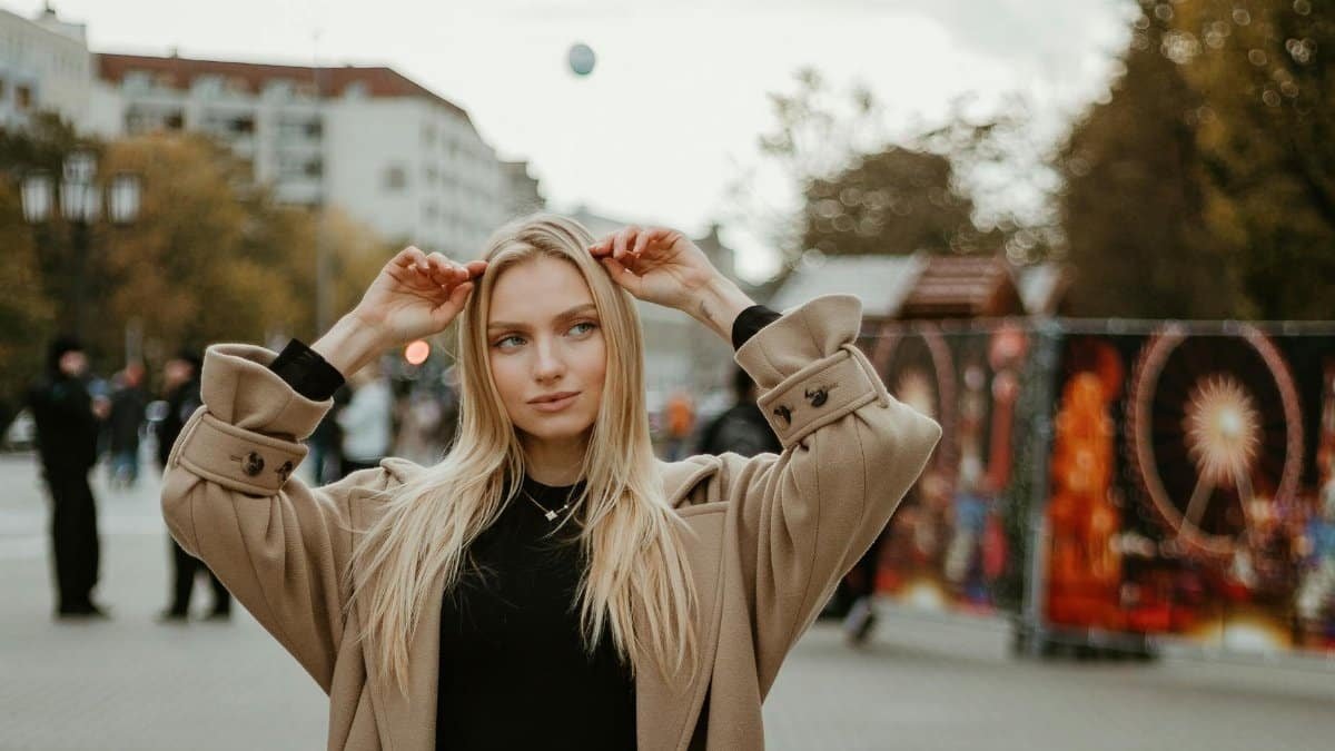 Young woman in a stylish coat poses in a city during autumn, capturing urban fashion vibes.