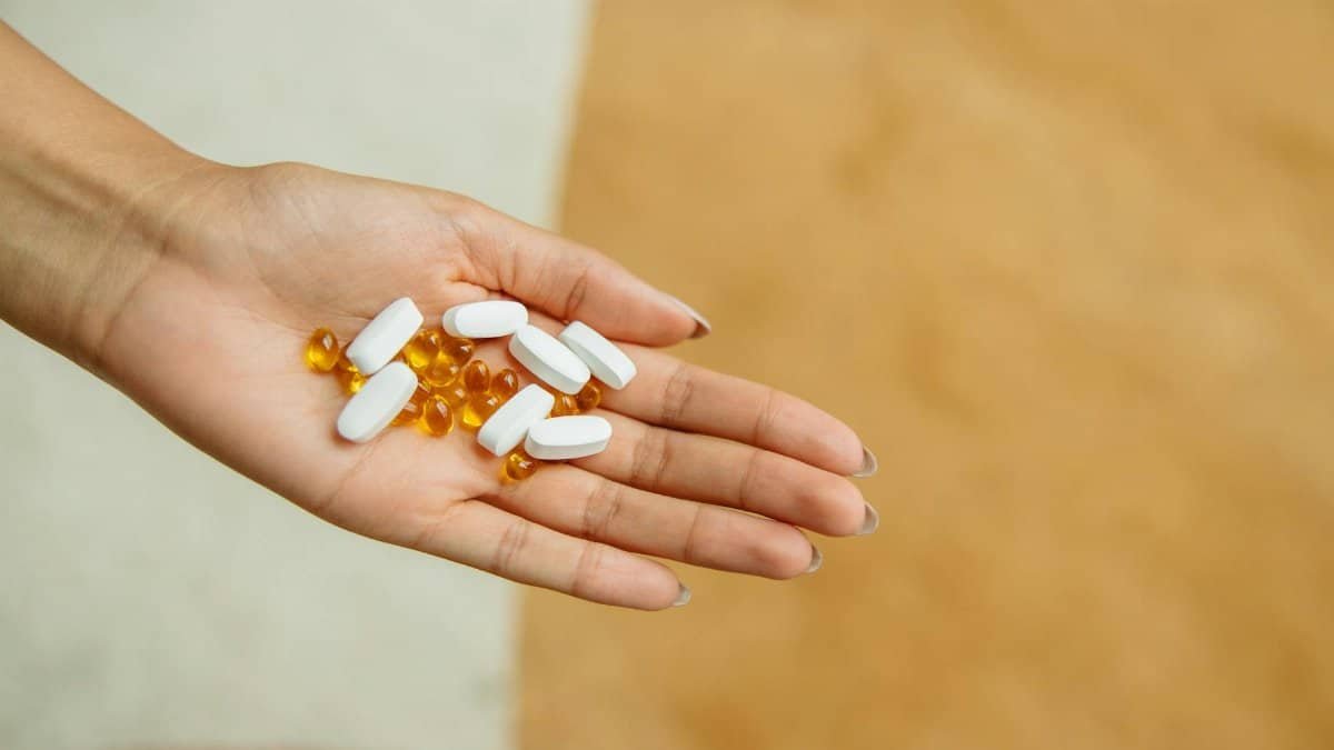 Close-up of a hand holding white pills and yellow capsules, symbolizing health and wellness.