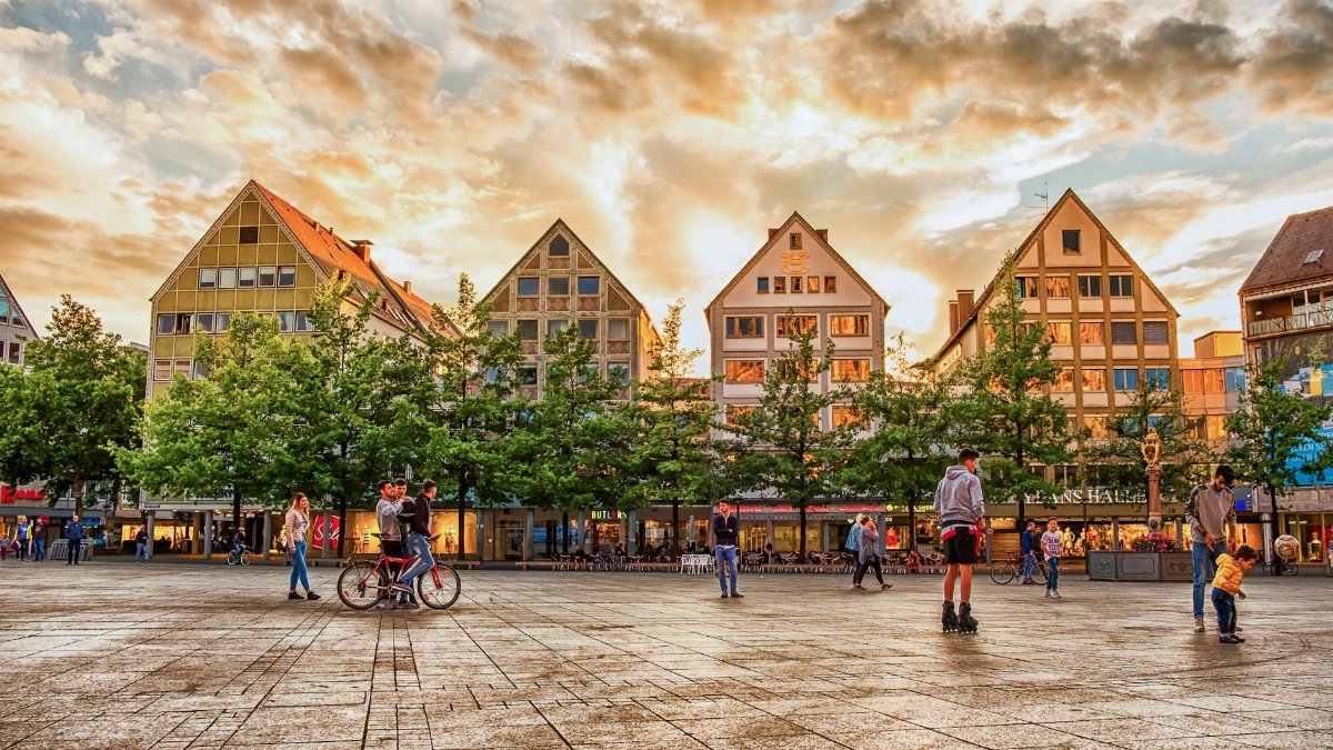 A vibrant town square in Ulm, Germany, with people enjoying the sunset.
