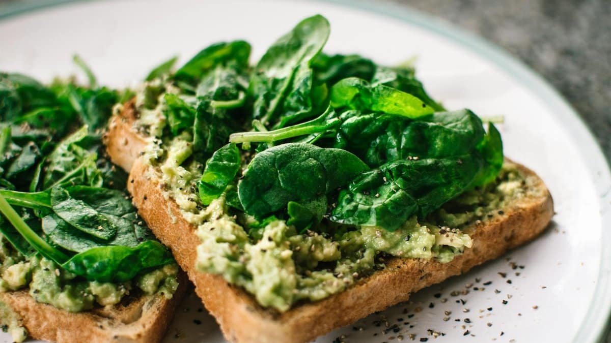 Close-up of a homemade avocado and spinach sandwich on whole grain toast.
