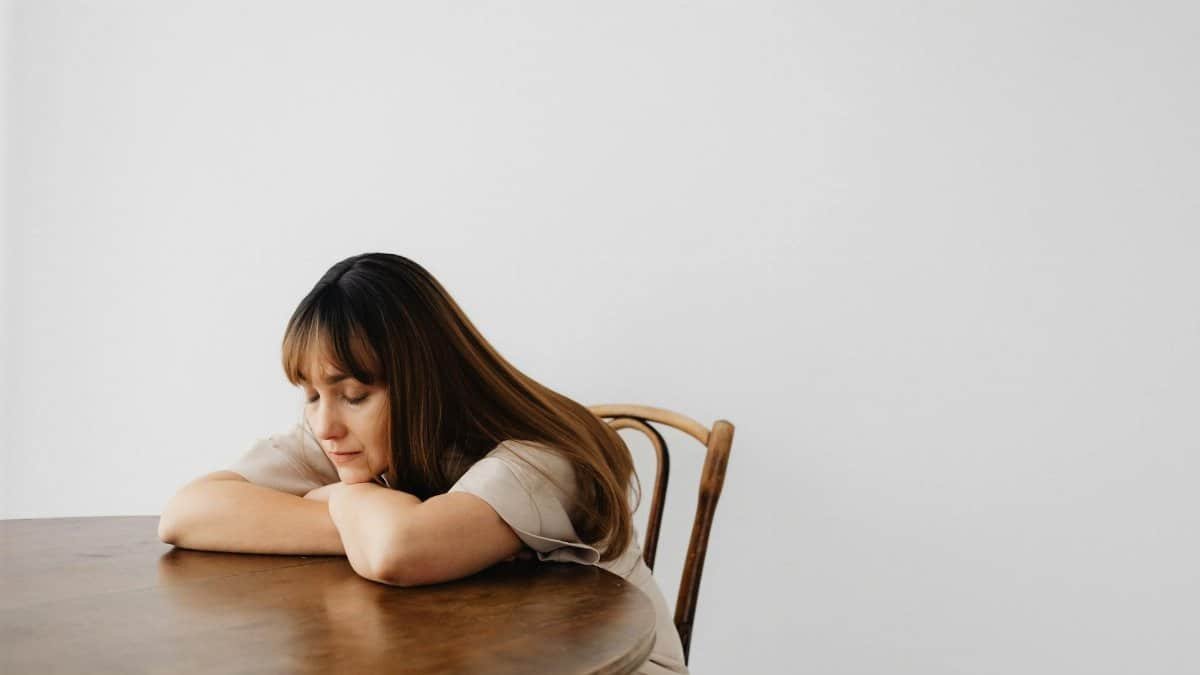 A calm and serene portrait of a woman resting with eyes closed at a wooden table.
