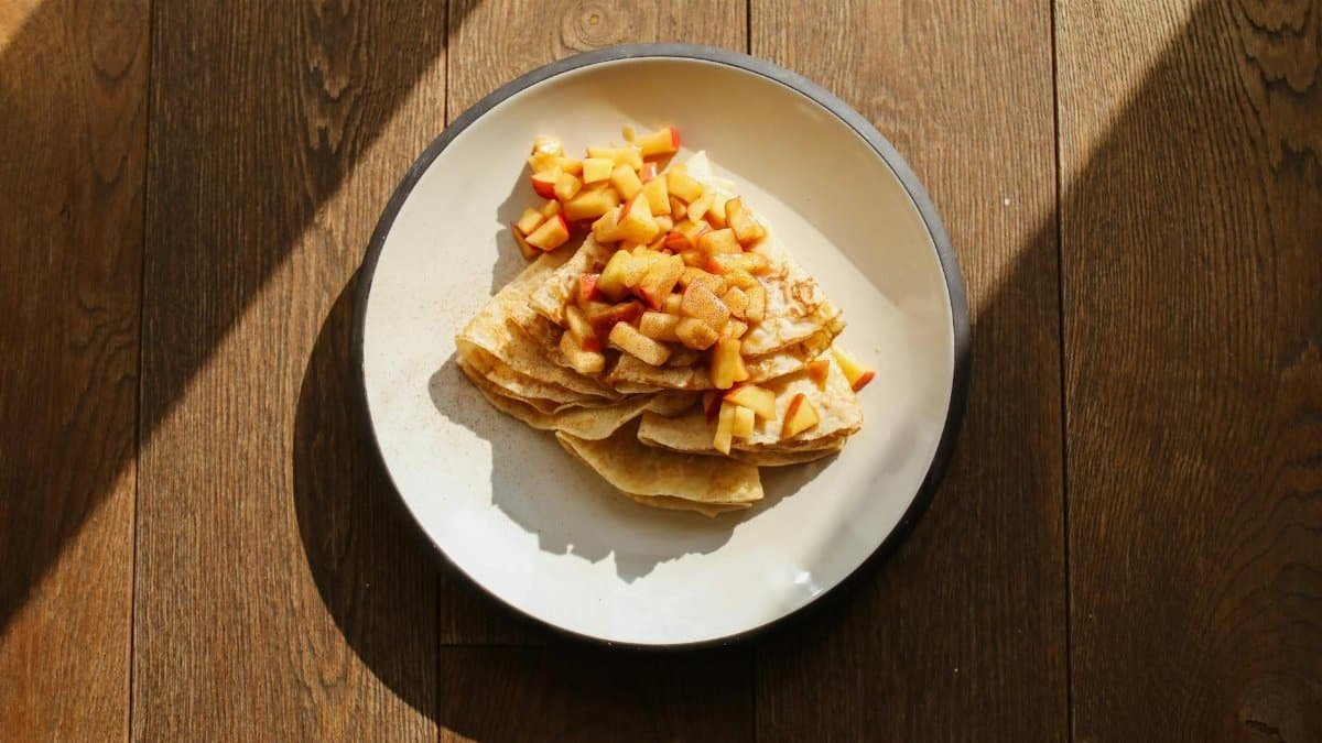 Delicious apple and cinnamon crepes served on a white plate with warm natural lighting.