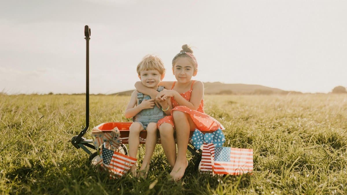 Two kids in a field with American flags, symbolizing summer and independence.