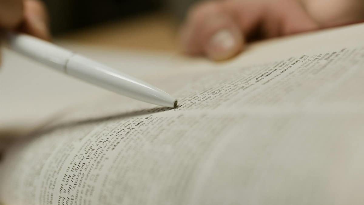 A person uses a pen to point at text in an open book, focusing on study or research.