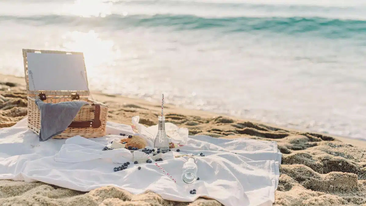 Peaceful seaside picnic setup with basket, croissant, and blueberries on a white blanket by the ocean.