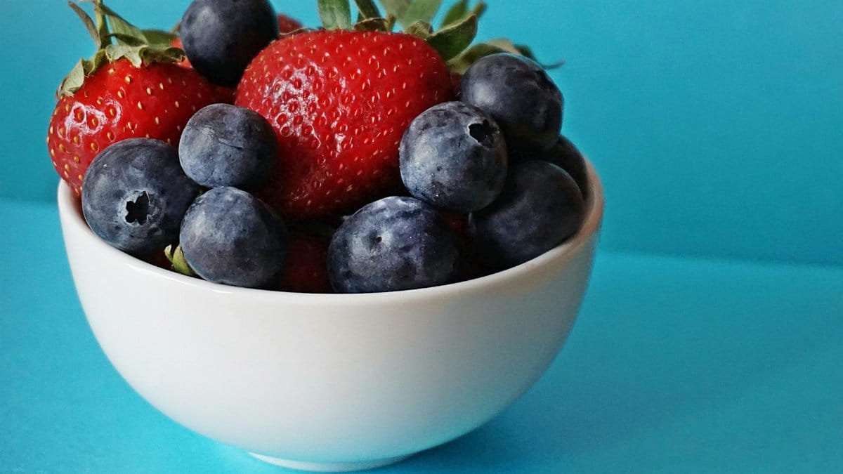 A vibrant mix of fresh strawberries and blueberries in a white bowl on a blue background.