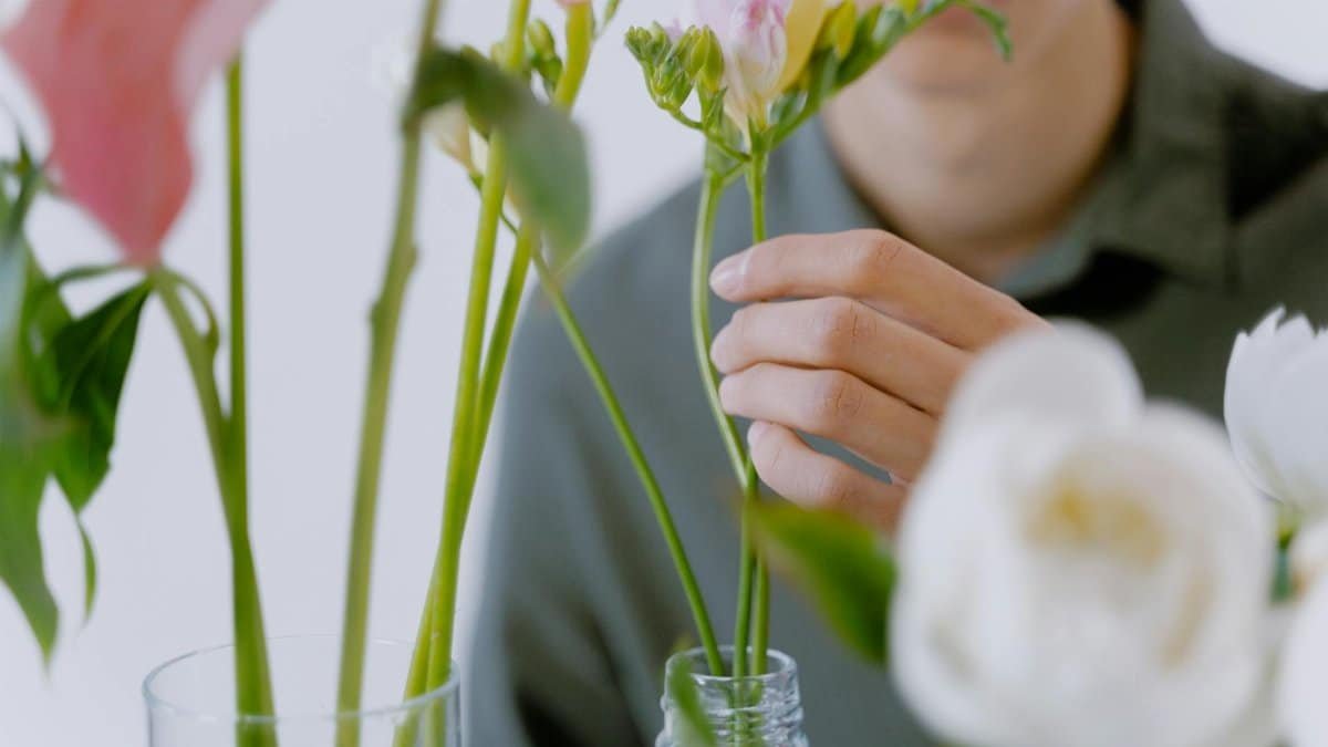 A person holding a flower stem, arranging vibrant blooms in vases.