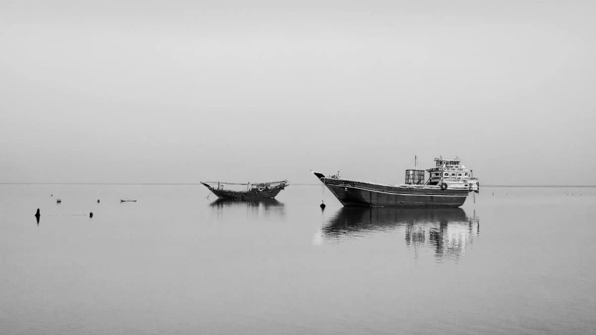 Serene black and white image of boats docked on calm sea waters, reflecting tranquility.