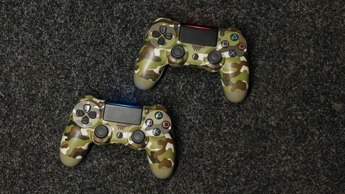 Close-up view of two camouflage-patterned gaming controllers on a textured surface.