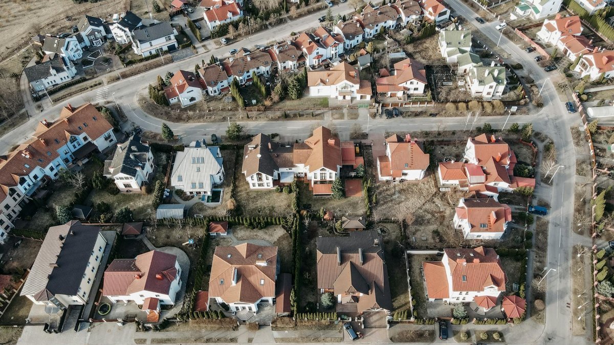 High-angle aerial view of urban residential area with red-roofed houses and winding roads.