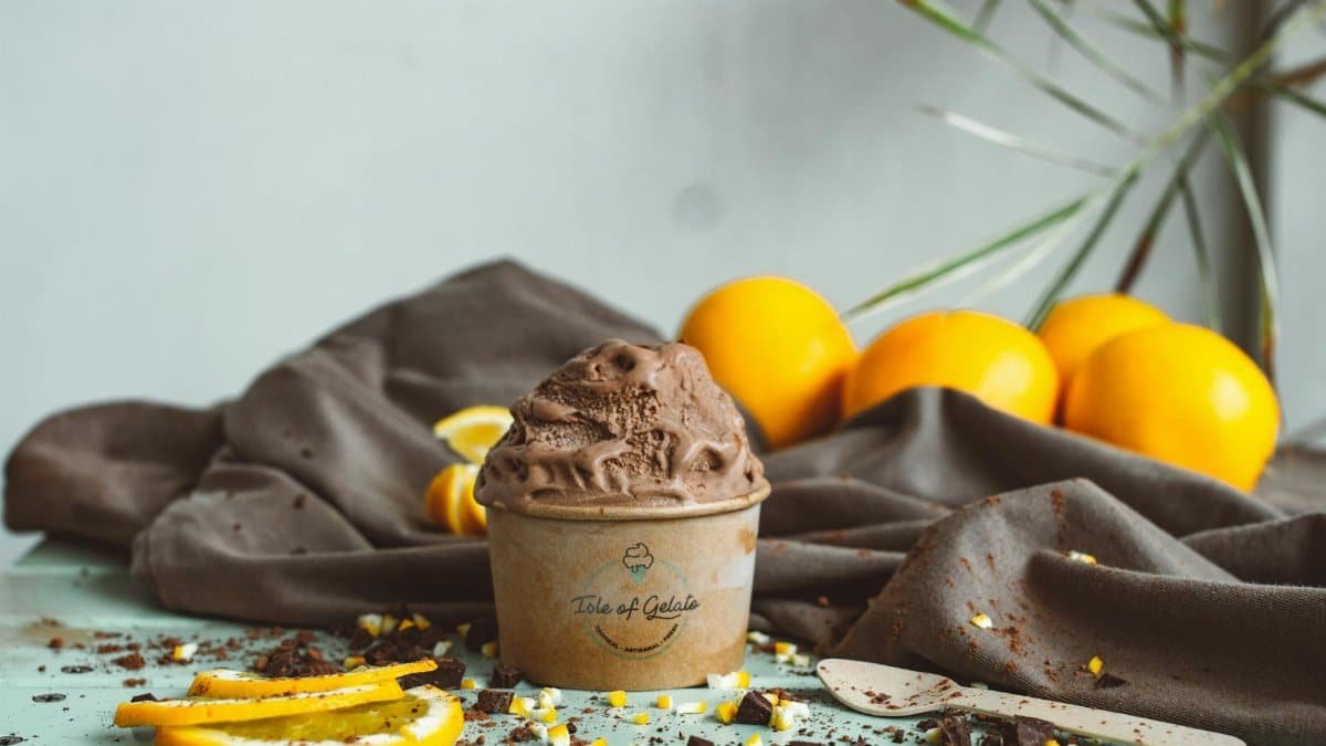 Delicious chocolate gelato in a paper cup with citrus decoration on a rustic setting.