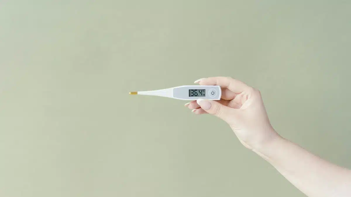 Hand holding a digital thermometer displaying 36.4°C on a light green background, minimalistic style.