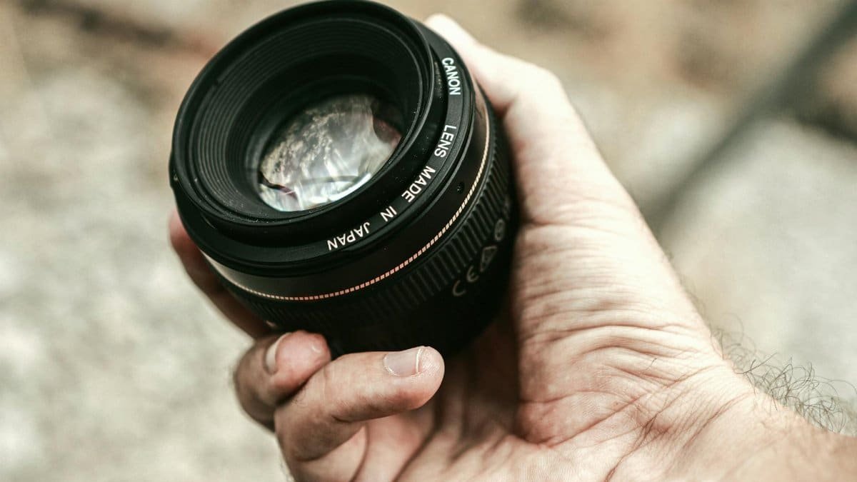 A close-up shot of a hand holding a camera lens in an outdoor setting.