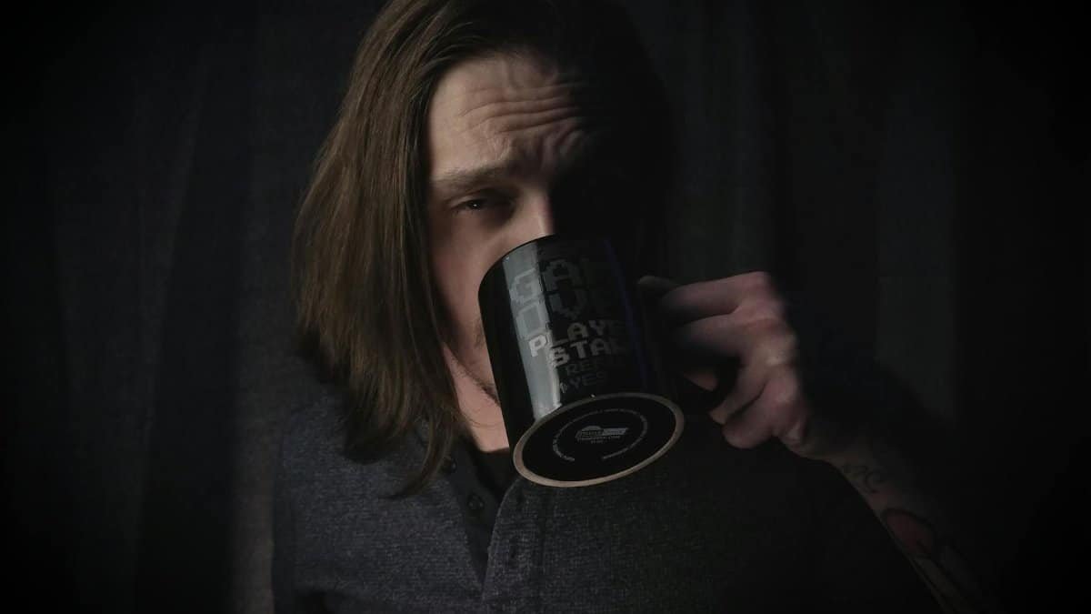 A moody portrait captures a man savoring a cup of coffee indoors.