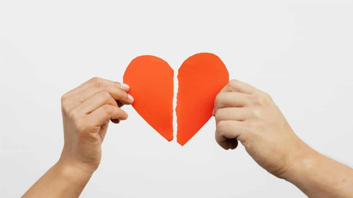 A close-up view of hands holding a torn red paper heart, symbolizing heartbreak or relationship issues.