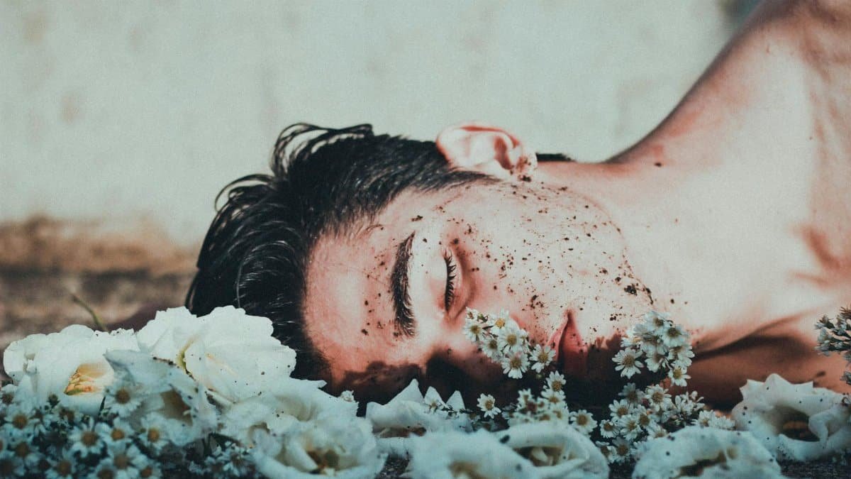 A contemplative image of a man lying among white flowers, conveying introspection.