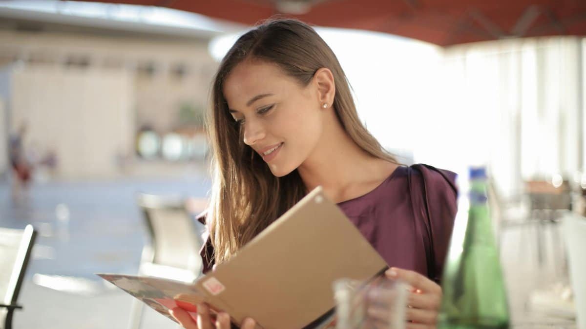 A smiling young woman reading a menu outdoors under parasols, enjoying a casual afternoon.