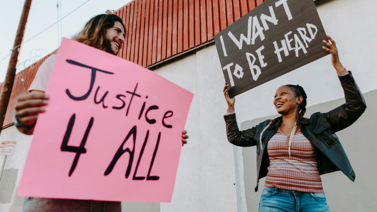 Two individuals holding protest signs advocating for justice and equality in an outdoor setting.