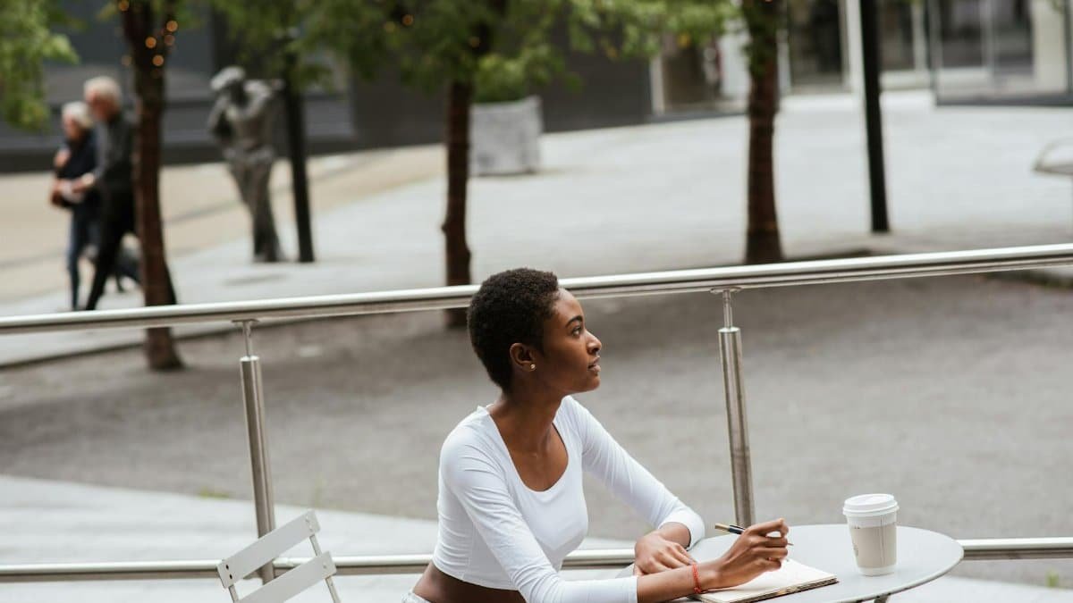 Woman enjoys coffee and notepad outdoors on urban terrace, relaxing and contemplating.