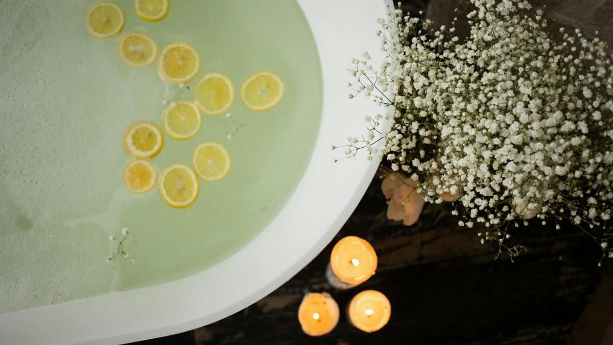 Overhead shot of a bath with lemon slices, candles, and flowers for a soothing spa ambiance.