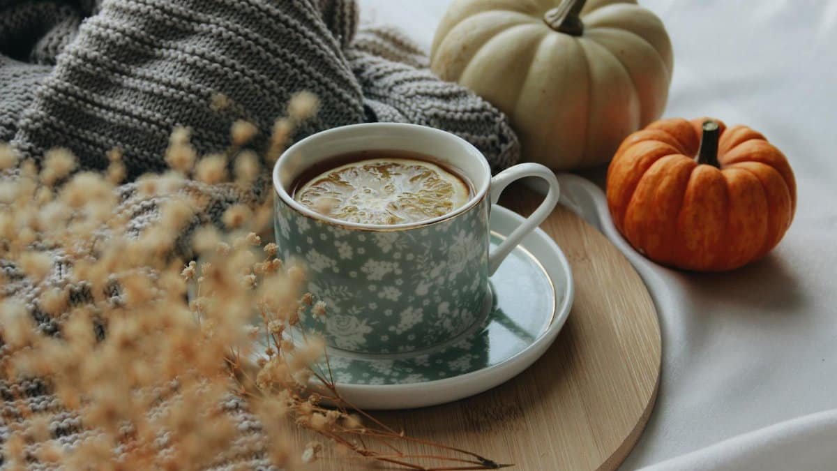 Warm autumn setting with a cup of tea, lemon slice, and decorative pumpkins on a wooden tray.