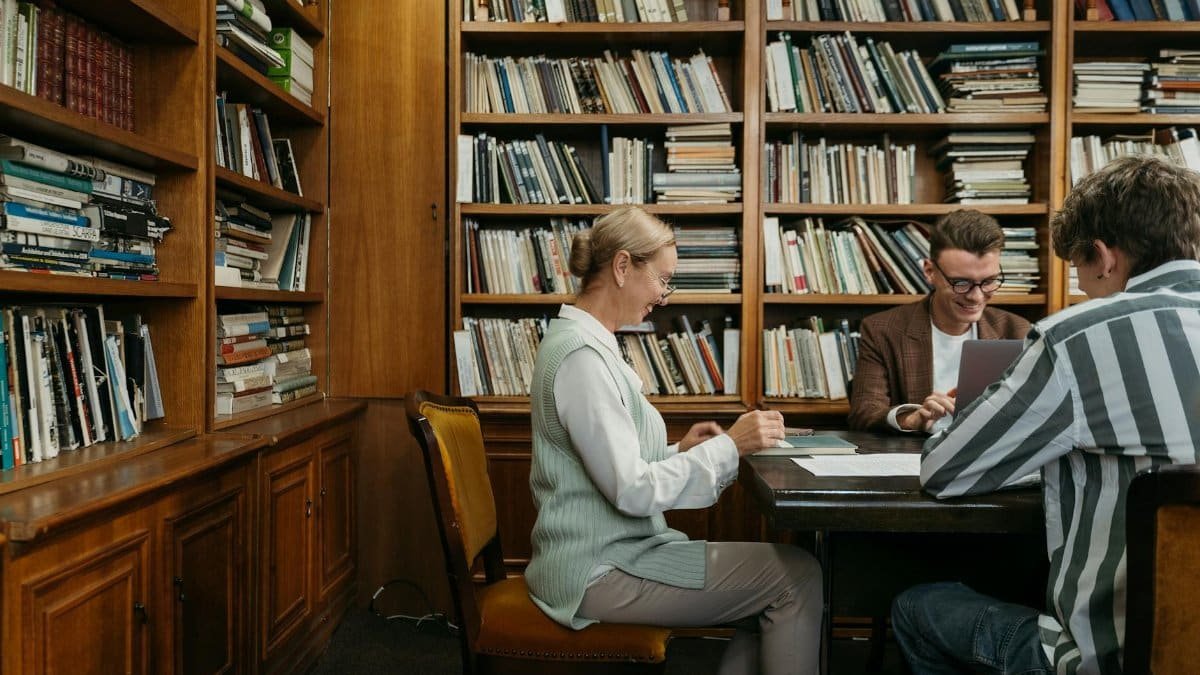 Group of students studying together in a cozy library setting with bookshelves around.