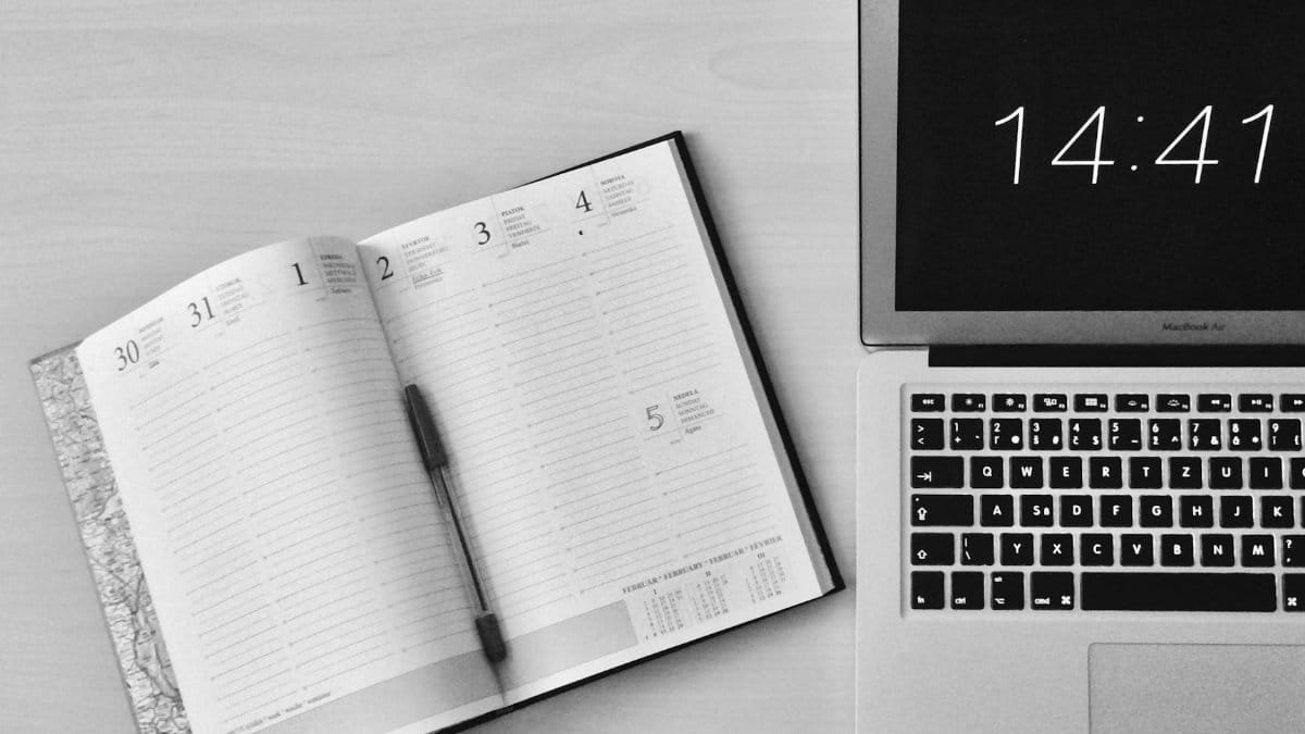 Minimalist office workspace with a notebook and MacBook Air showing 14:41 time.