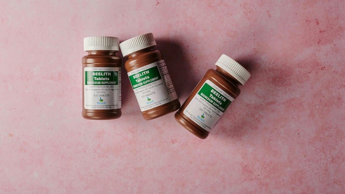 Three brown bottles of magnesium tablets on a soft pink background, ideal for health-themed content.