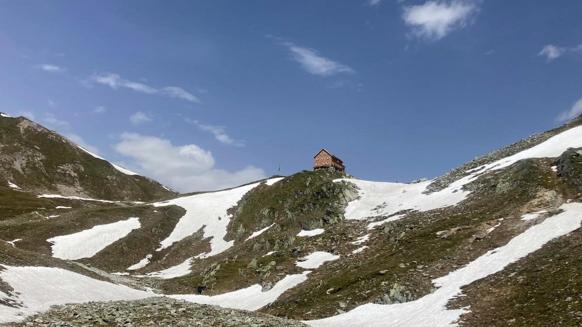 A solitary mountain hut nestled within a snowy alpine landscape under a clear blue sky.