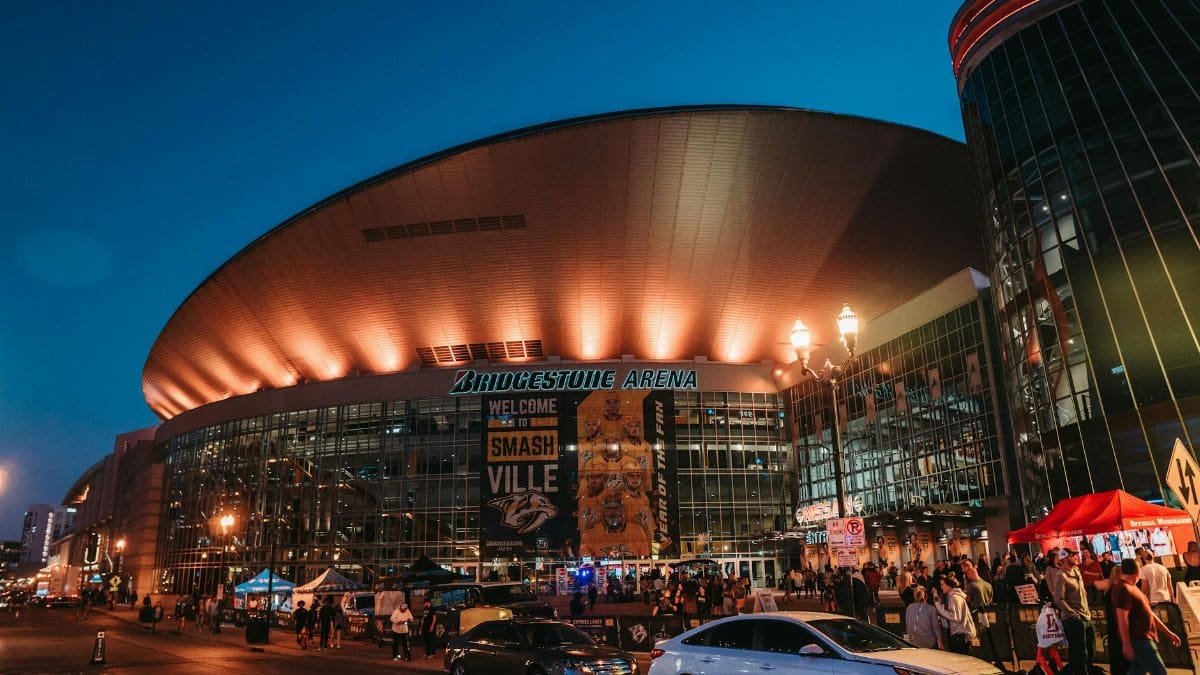 Exterior view of Bridgestone Arena at night in Nashville, Tennessee, with people gathered.