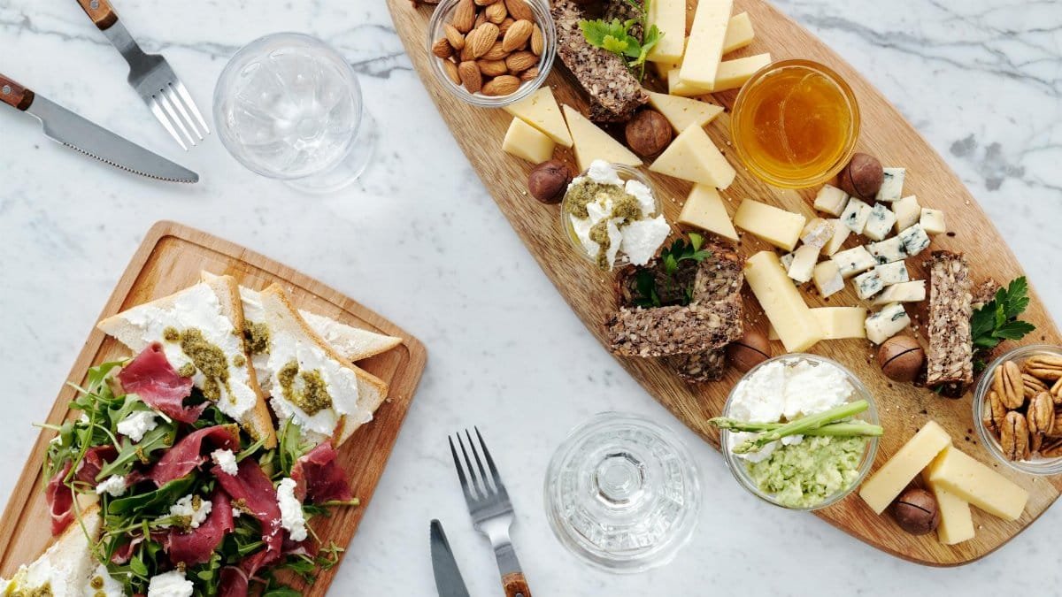 A top view of assorted cheeses, nuts, meats, and bread on a wooden charcuterie board.