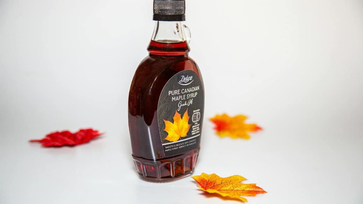 Close-up of a Canadian maple syrup bottle with colorful autumn leaves on white background.