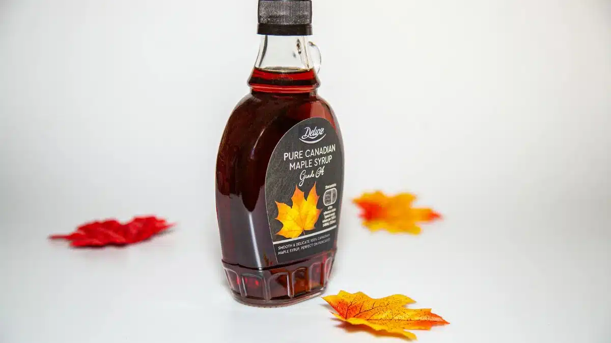 Close-up of a Canadian maple syrup bottle with colorful autumn leaves on white background.