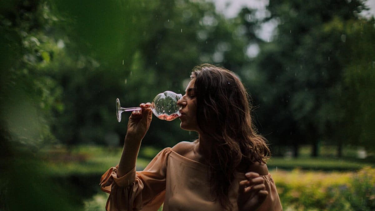 Elegant woman drinking wine in a lush garden setting, enjoying a tranquil moment.