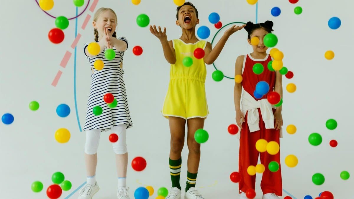 Three joyful kids play with colorful balls in a playful indoor setting, expressing happiness and fun.