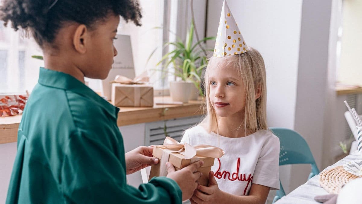 A joyful moment of children exchanging a gift during a birthday celebration indoors, highlighting friendship and fun.