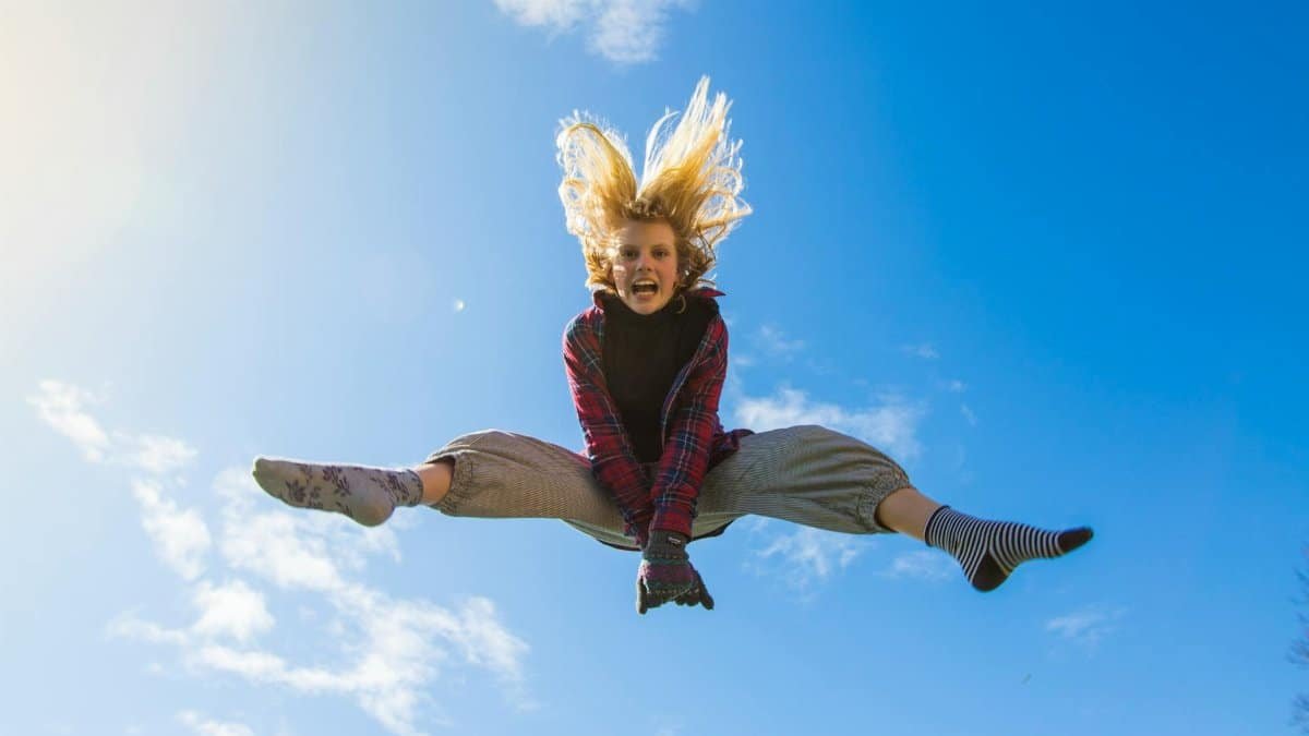 A girl energetically jumping under a clear blue sky, expressing freedom and joy.