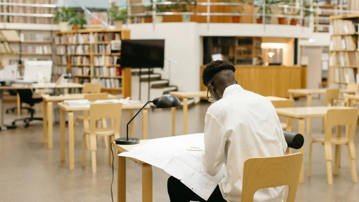 A student studying at a desk in a modern library with bookshelves and open space.