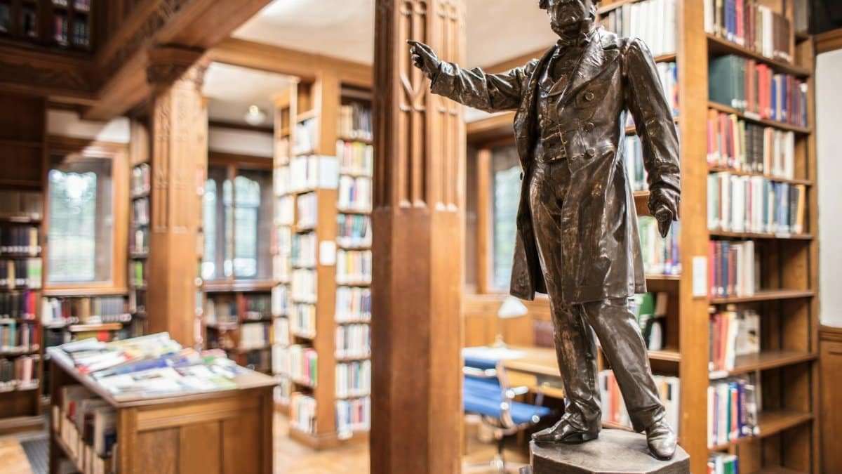 A historic statue inside a classic library in Hawarden, Wales, surrounded by shelves of books.