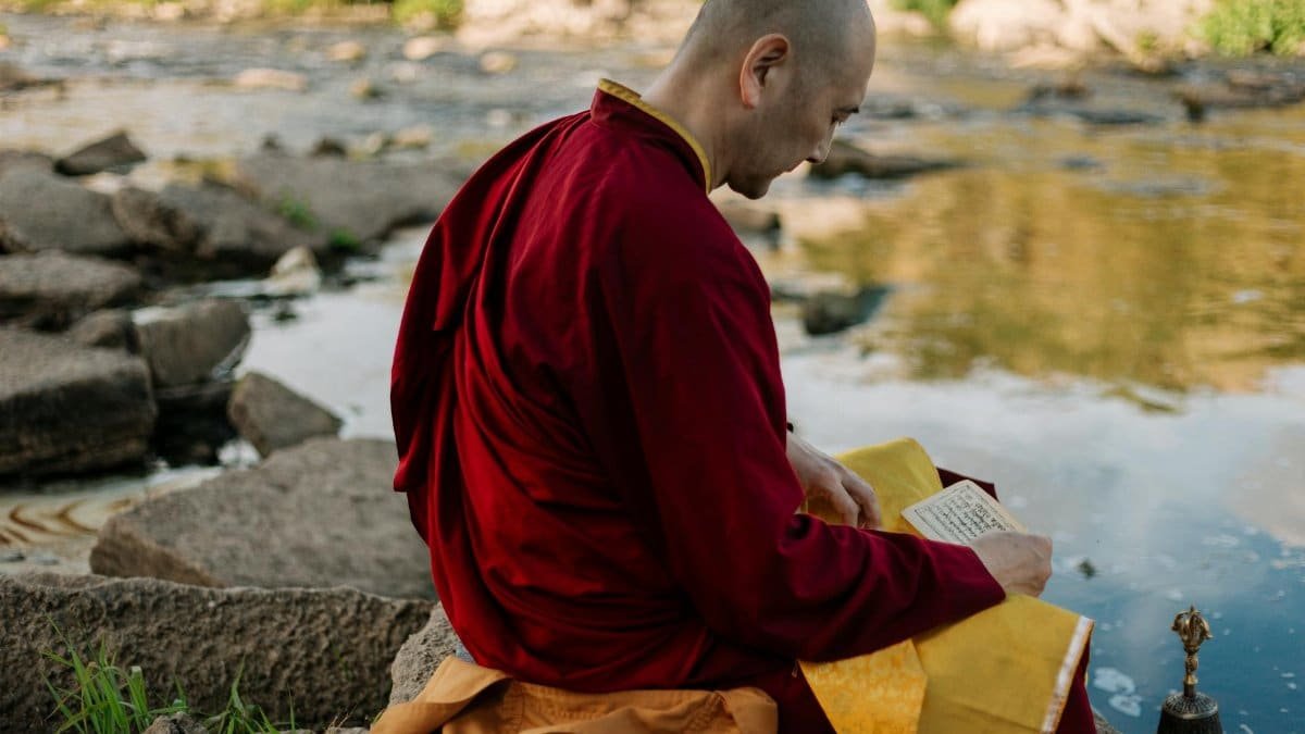 A Buddhist monk in deep meditation by a tranquil riverside setting during autumn.