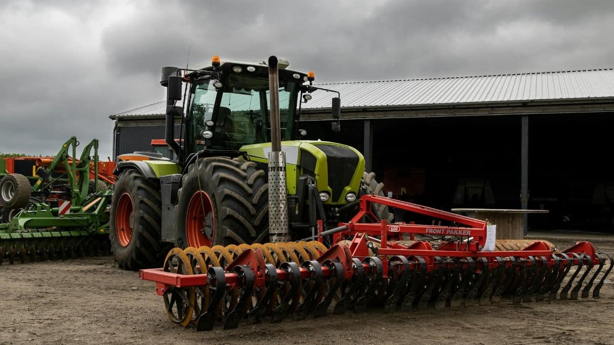 A modern tractor with agricultural machinery in a rural outdoor setting.