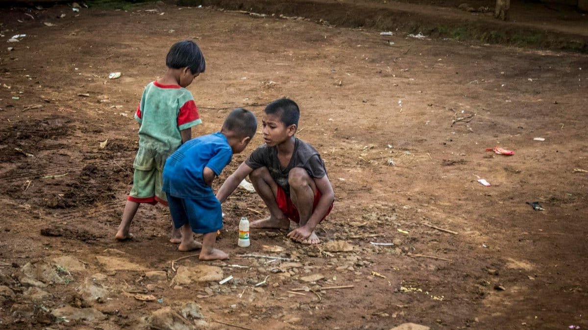 Three young children playing on a dirt path, depicting playful interaction in a rural setting.