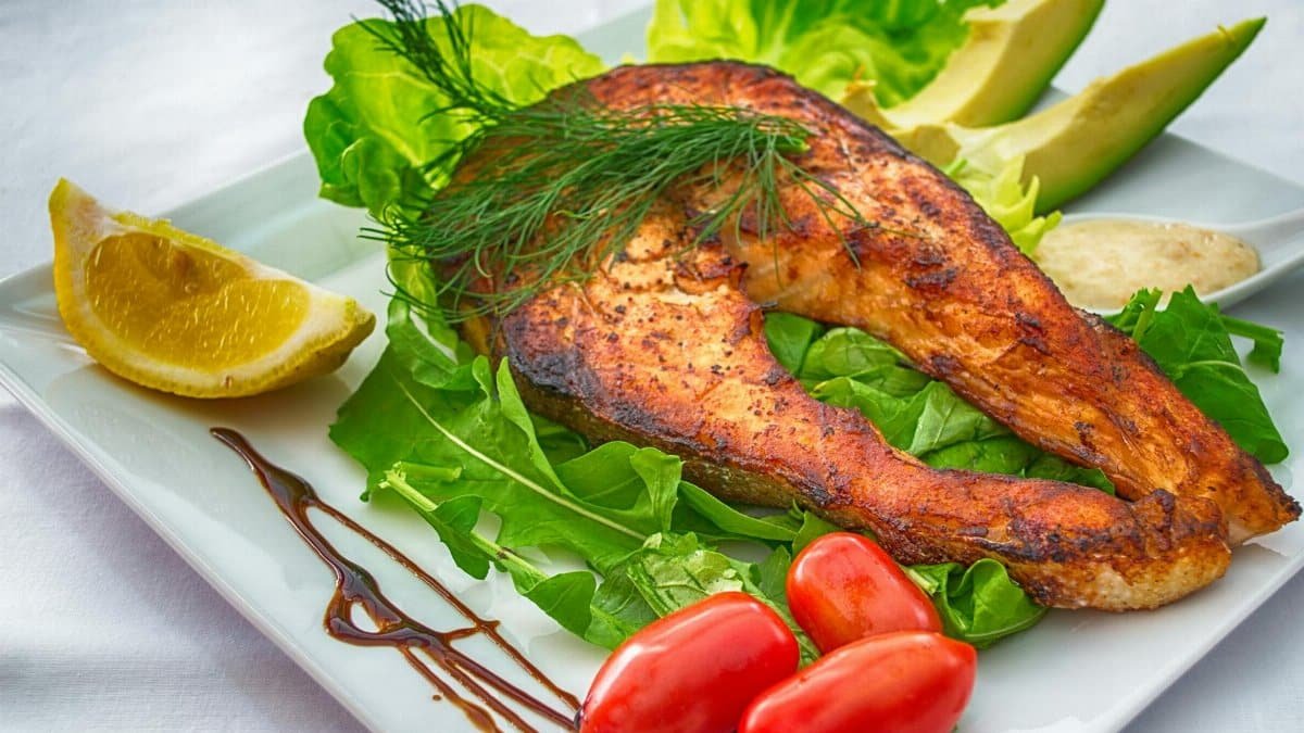 Delicious grilled salmon served with fresh vegetables and herbs on a white plate.