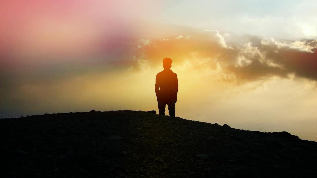 A silhouette of a person standing on a hill with a colorful sunset background, evoking calm and reflection.