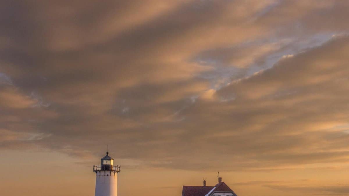 Dramatic sunset sky over Cape Cod lighthouse in Provincetown, Massachusetts, creating a serene coastal scene.