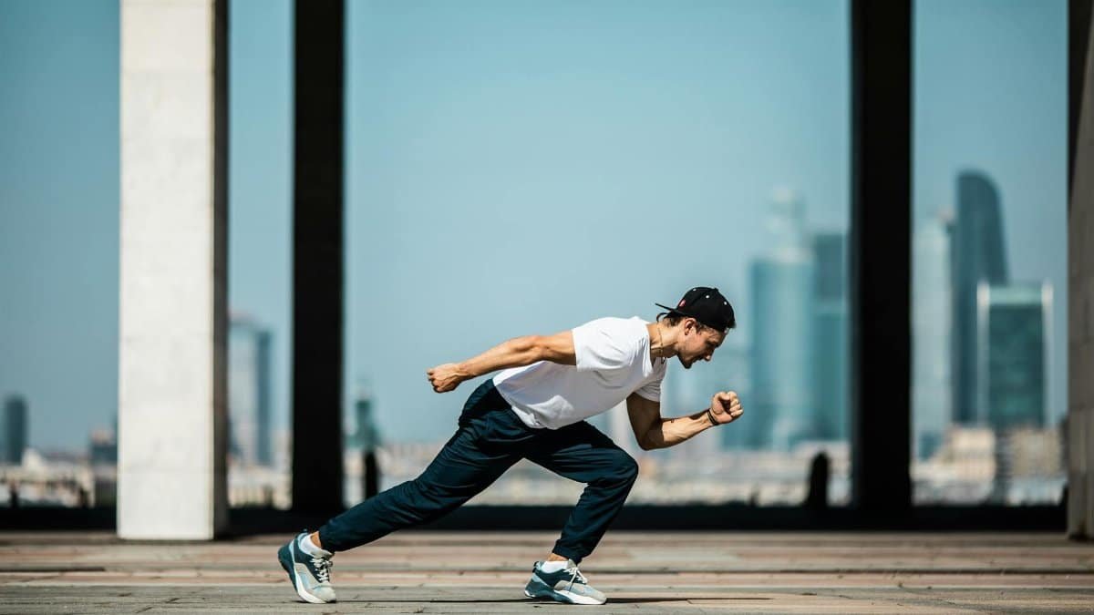 Dynamic shot of a young man sprinting outdoors in an urban setting with skyscrapers in the background.