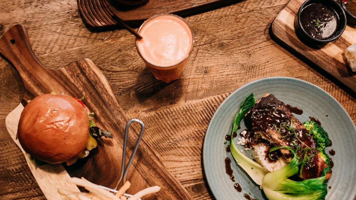 Top view of a meal with gourmet burger, stir fry dish, and a smoothie on a rustic table.